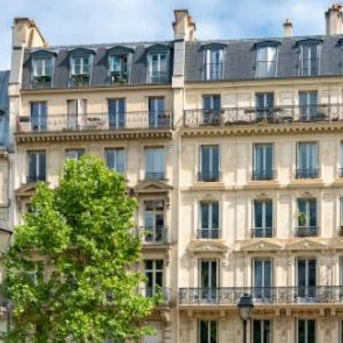 Bâtiment haussmannien avec balcons et fenêtres, entouré d'un arbre.