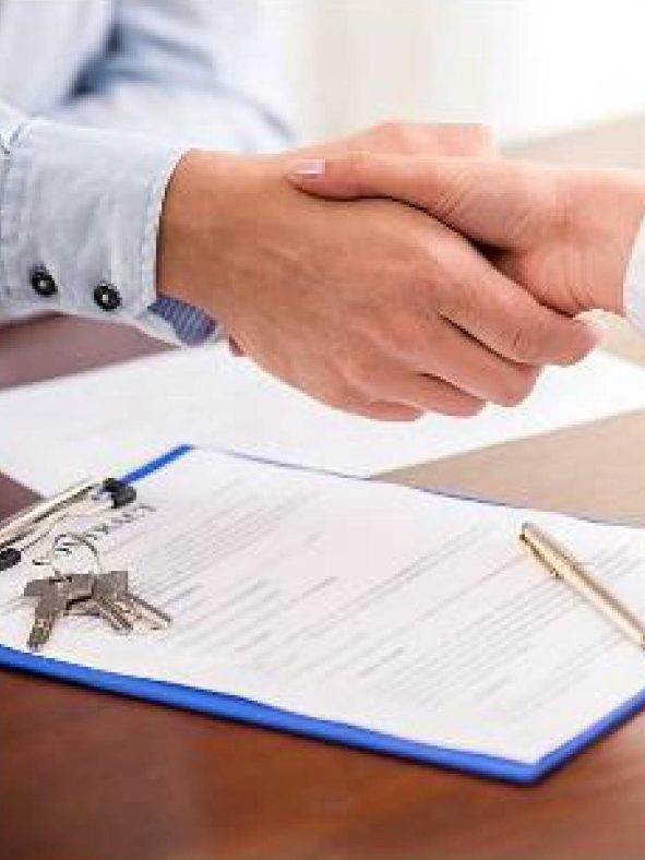 Deux mains se serrent au-dessus d'un document et de clés posées sur une table.