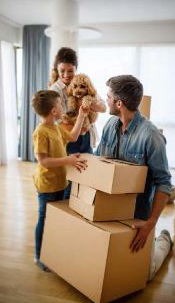 Famille souriante déballant des cartons avec un chien dans un nouvel intérieur.