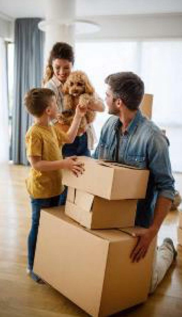 Une famille souriante avec un chien et des cartons dans un espace de vie.